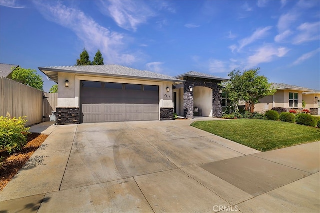 prairie-style home with a front yard, driveway, stone siding, stucco siding, and fence