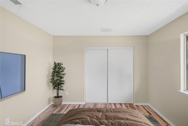 bedroom featuring baseboards, wood finished floors, a textured ceiling, and a closet