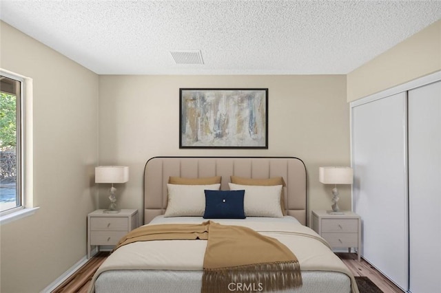 bedroom with visible vents, wood finished floors, a textured ceiling, and a closet