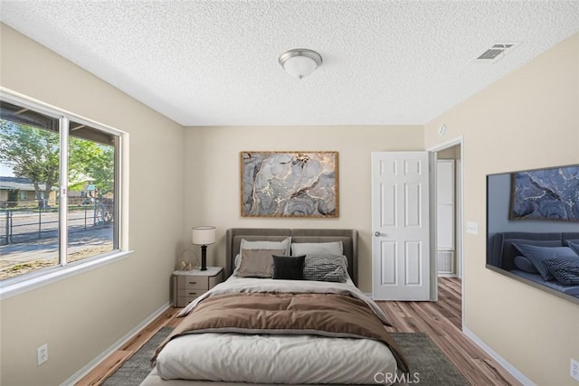 bedroom featuring baseboards, visible vents, wood finished floors, and a textured ceiling