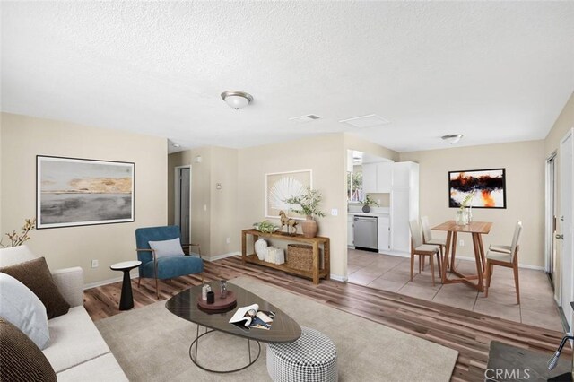 living area with a textured ceiling, visible vents, baseboards, and light wood-type flooring