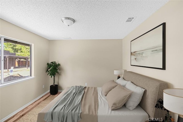 bedroom featuring a textured ceiling, wood finished floors, visible vents, and baseboards