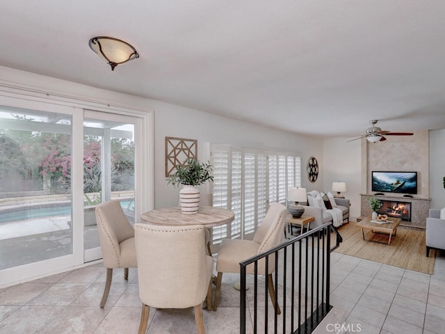 dining room with light tile patterned floors, a large fireplace, ceiling fan, and a healthy amount of sunlight