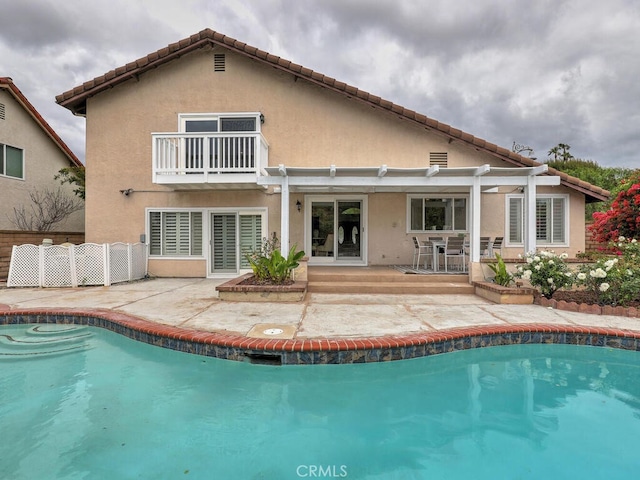 back of house with a balcony, a patio, an outdoor pool, a pergola, and stucco siding