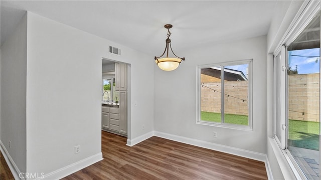 unfurnished dining area featuring visible vents, a sink, baseboards, and dark wood-type flooring