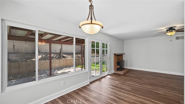 interior space with a ceiling fan, a lit fireplace, visible vents, wood finished floors, and baseboards