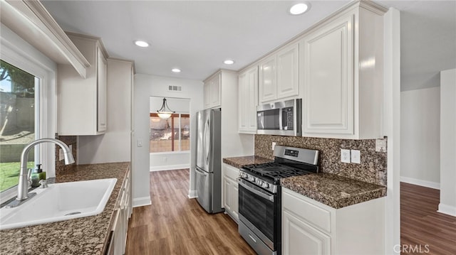 kitchen featuring decorative backsplash, wood finished floors, a sink, baseboards, and stainless steel appliances