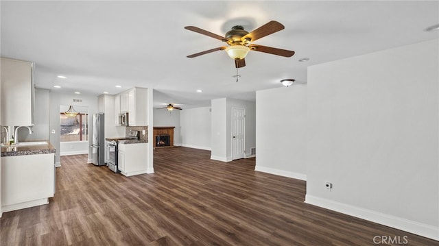 unfurnished living room with baseboards, a fireplace, a ceiling fan, and dark wood-style flooring