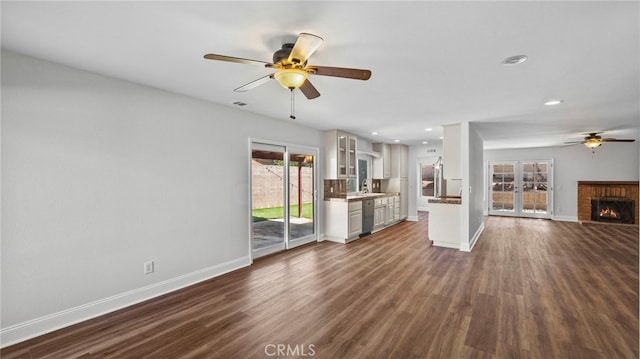 unfurnished living room featuring a ceiling fan, baseboards, dark wood-type flooring, and a fireplace