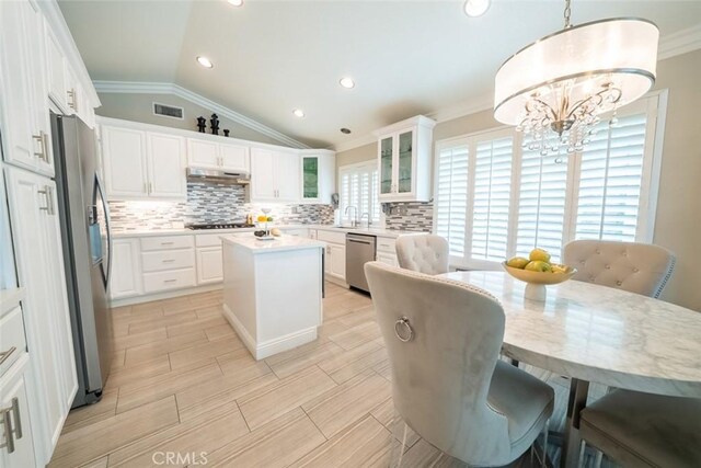 kitchen with appliances with stainless steel finishes, a center island, vaulted ceiling, ornamental molding, and under cabinet range hood