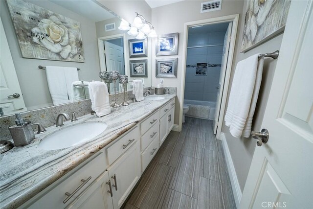 full bathroom with a sink, toilet, double vanity, and visible vents