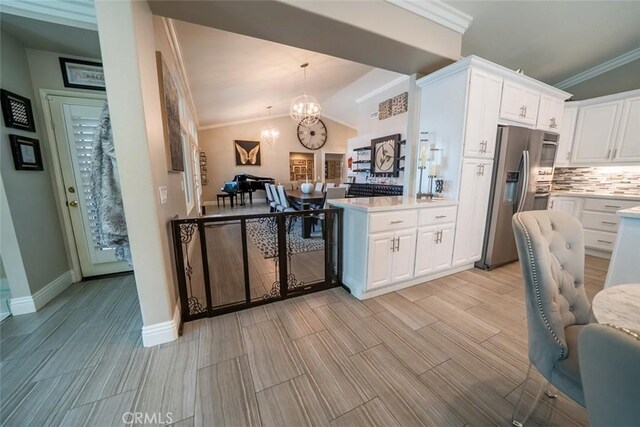 kitchen featuring backsplash, light countertops, stainless steel fridge with ice dispenser, a notable chandelier, and white cabinetry