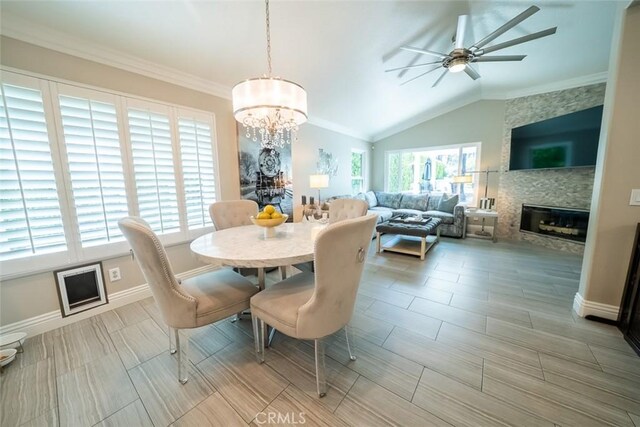 dining area featuring a fireplace, baseboards, ceiling fan with notable chandelier, lofted ceiling, and ornamental molding