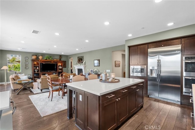 21609 Lucas Ct, Saugus, CA 91390 - kitchen with dark brown cabinets, built in appliances, a kitchen island, a lit fireplace, and dark wood-style floors