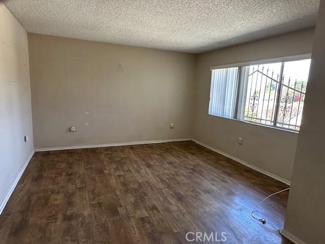 unfurnished room featuring a textured ceiling, wood finished floors, and baseboards