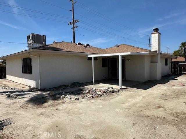 back of house featuring a patio area, central AC unit, a chimney, stucco siding, and fence