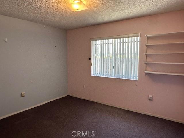 unfurnished room featuring a textured ceiling and dark colored carpet