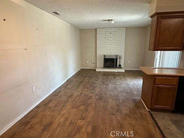 unfurnished living room with a fireplace, dark wood-type flooring, visible vents, baseboards, and a textured ceiling