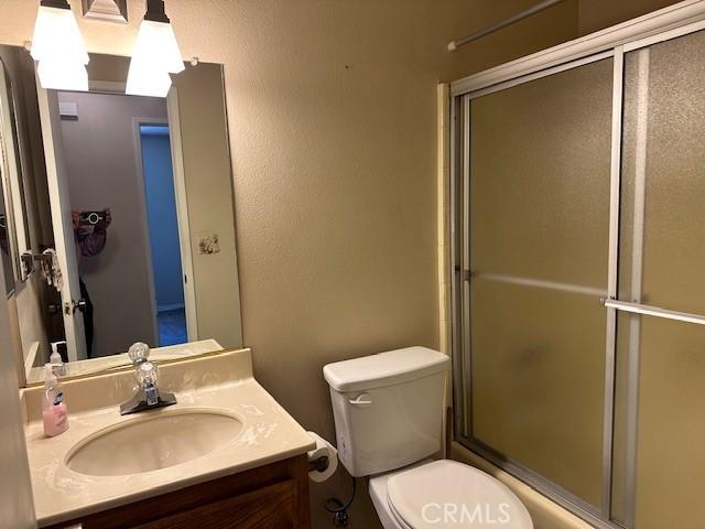full bathroom with toilet, a shower with door, and vanity