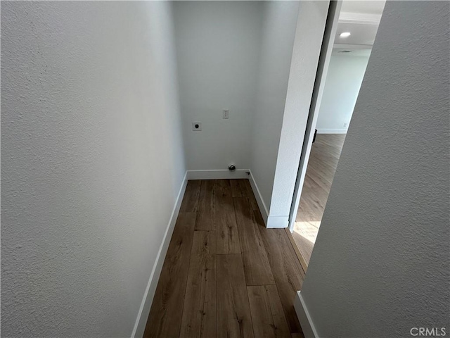 hall featuring a textured wall, dark wood-style floors, and baseboards