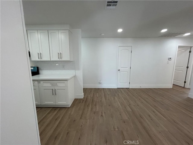 interior space with wood finished floors, white cabinetry, light countertops, baseboards, and visible vents