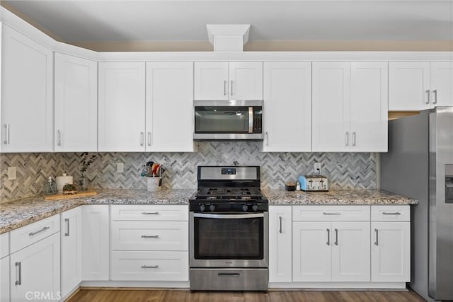 kitchen featuring light stone countertops, white cabinets, appliances with stainless steel finishes, and tasteful backsplash