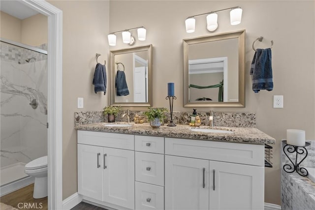 full bathroom with double vanity, toilet, a marble finish shower, and a sink