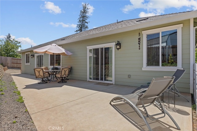 rear view of house with fence, a shingled roof, and a patio area