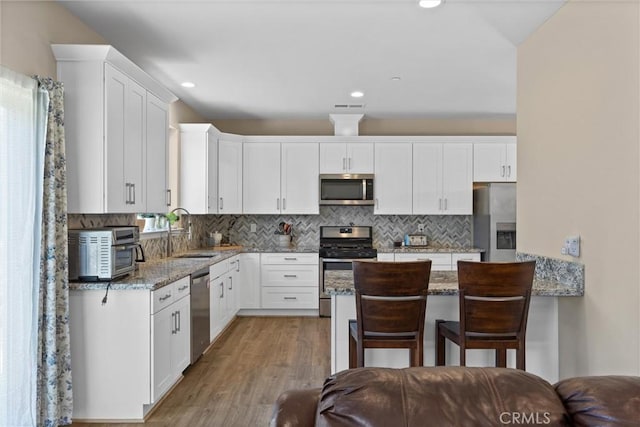 kitchen featuring tasteful backsplash, white cabinets, a sink, stainless steel appliances, and light stone countertops