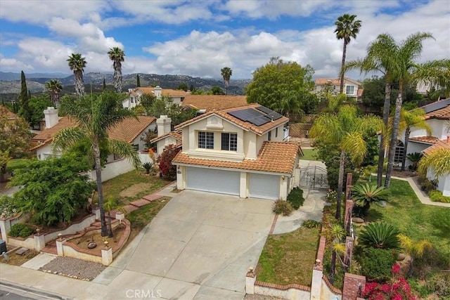 mediterranean / spanish-style home featuring a gate, a tiled roof, roof mounted solar panels, concrete driveway, and stucco siding