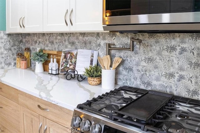 room details with appliances with stainless steel finishes, light stone countertops, and white cabinets