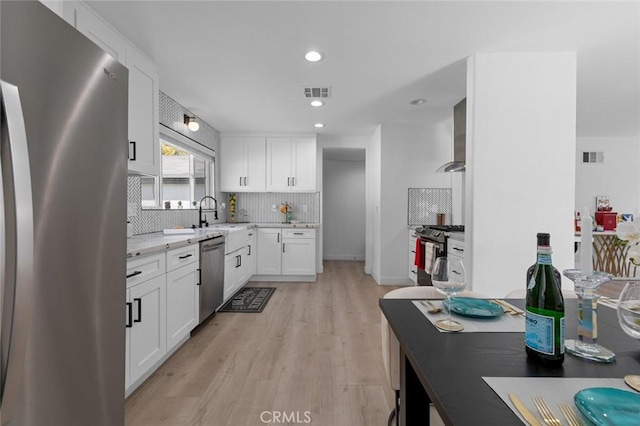 kitchen with wall chimney range hood, a sink, appliances with stainless steel finishes, visible vents, and light stone countertops