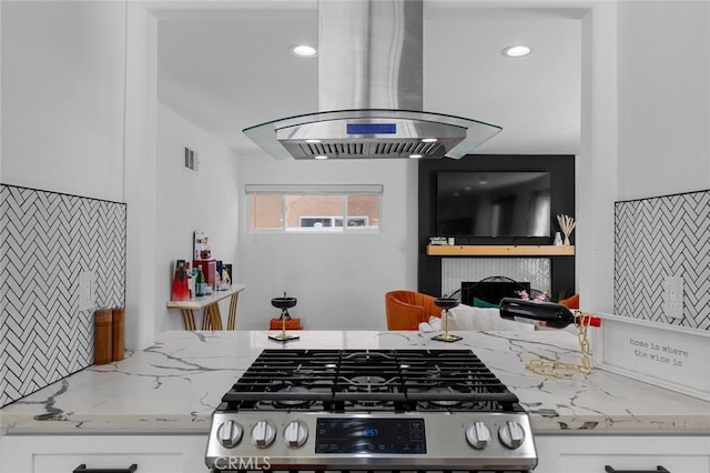 kitchen with white cabinetry, island range hood, light stone counters, and stainless steel range with gas cooktop
