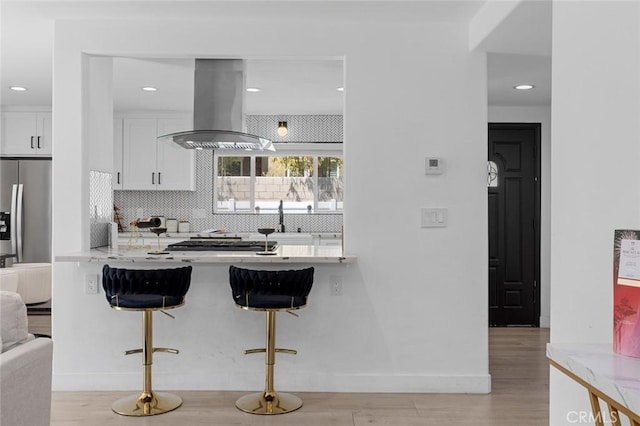 kitchen featuring a kitchen breakfast bar, tasteful backsplash, white cabinets, appliances with stainless steel finishes, and island exhaust hood