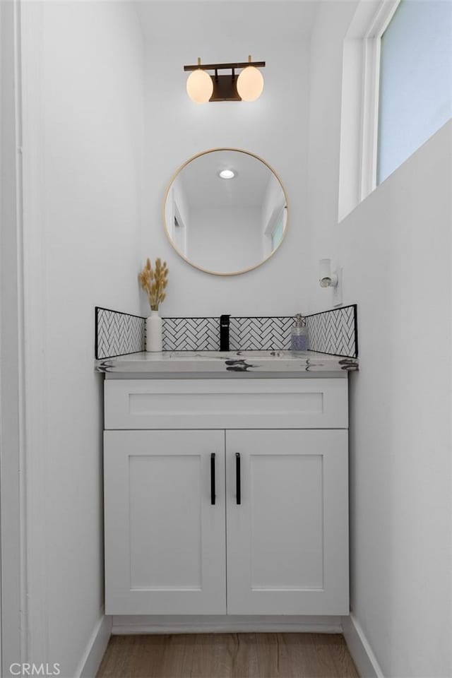 bathroom featuring baseboards, tasteful backsplash, wood finished floors, and vanity