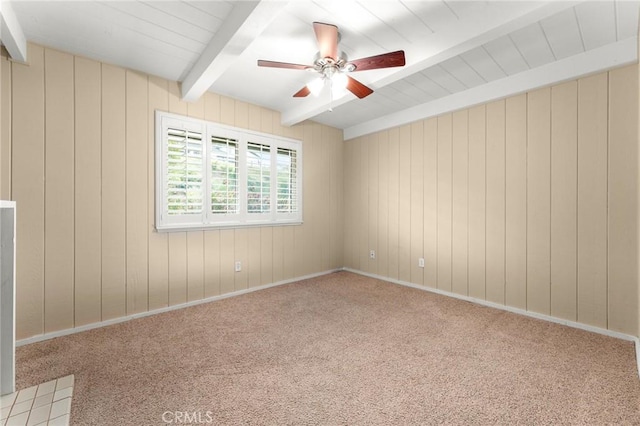 unfurnished room featuring a ceiling fan, wood walls, beam ceiling, and carpet