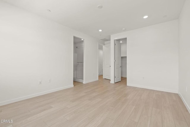 unfurnished bedroom featuring a walk in closet, baseboards, a closet, light wood-style floors, and recessed lighting