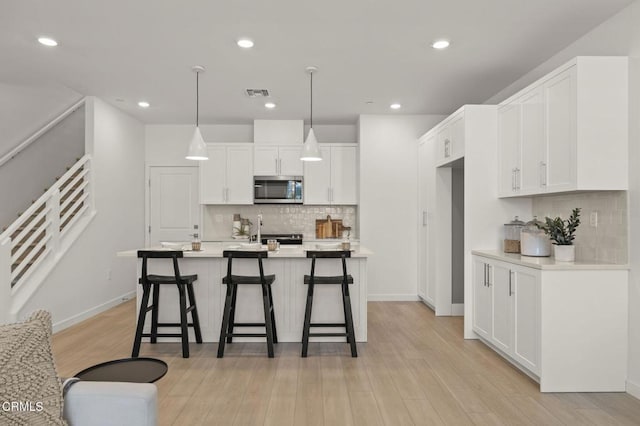 kitchen featuring tasteful backsplash, stainless steel microwave, white cabinetry, and visible vents