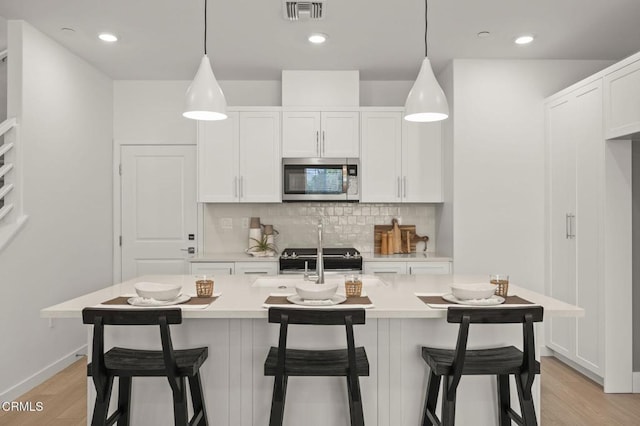 kitchen featuring light countertops, light wood-style flooring, stainless steel microwave, and tasteful backsplash