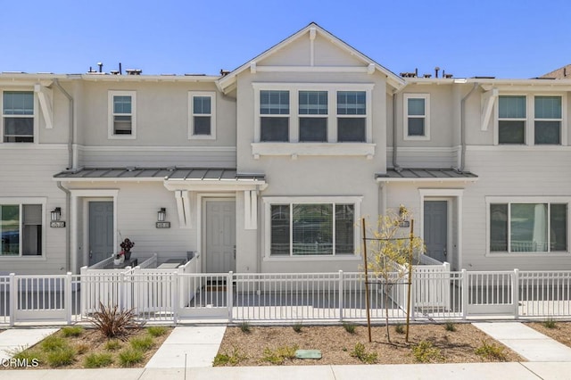 multi unit property featuring a fenced front yard, stucco siding, a gate, a standing seam roof, and metal roof