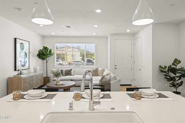 kitchen with a sink, light countertops, recessed lighting, open floor plan, and wood finished floors
