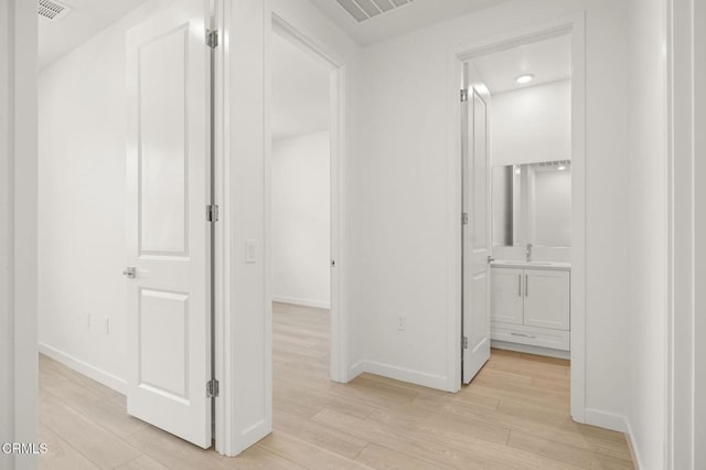 hall featuring a sink, baseboards, light wood-style flooring, and visible vents