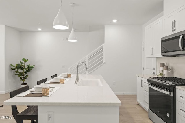 kitchen featuring appliances with stainless steel finishes, a sink, light countertops, light wood-style flooring, and white cabinetry