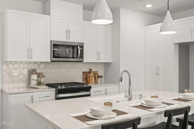 kitchen with appliances with stainless steel finishes, a breakfast bar, light countertops, white cabinetry, and decorative backsplash