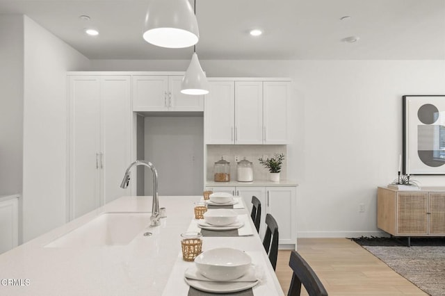 kitchen with light wood-type flooring, a sink, light countertops, recessed lighting, and white cabinetry