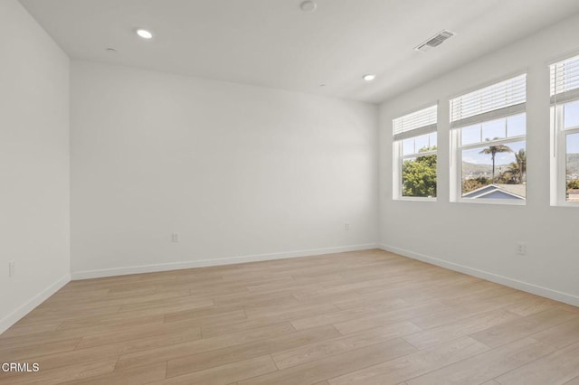 unfurnished room featuring light wood-style floors, baseboards, a wealth of natural light, and visible vents