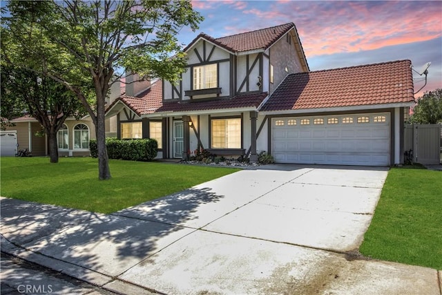 english style home featuring a tiled roof, driveway, a garage, a yard, and stucco siding