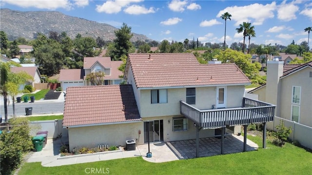 rear view of property featuring a tiled roof, a yard, a patio, a deck with mountain view, and stucco siding