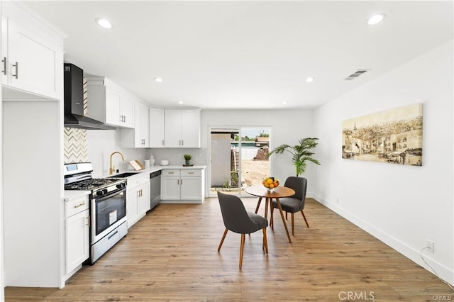 11445 Saticoy St, North Hollywood, CA 91605 - kitchen featuring stainless steel appliances, wall chimney range hood, a sink, light countertops, and white cabinetry