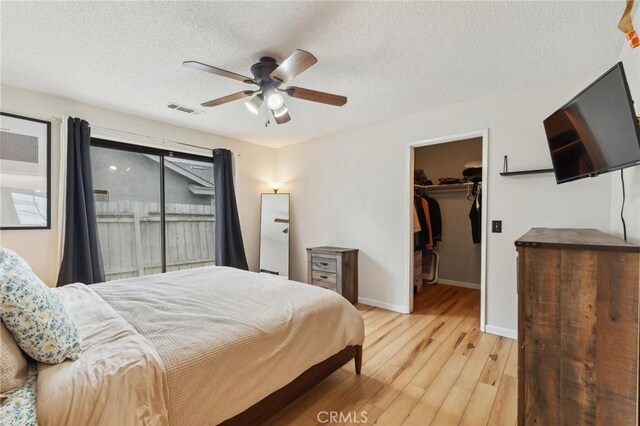 1045 Clover Ln, Hanford, CA 93230 - bedroom with light wood finished floors, a walk in closet, a textured ceiling, baseboards, and ceiling fan